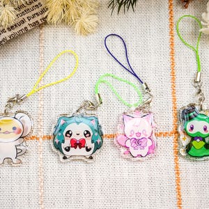 May include: Four colorful acrylic charms with cartoon animal designs. Each charm has a different character, including a white creature, a blue hedgehog, a pink cat, and a green ninja. Each charm has a colored loop for attachment.