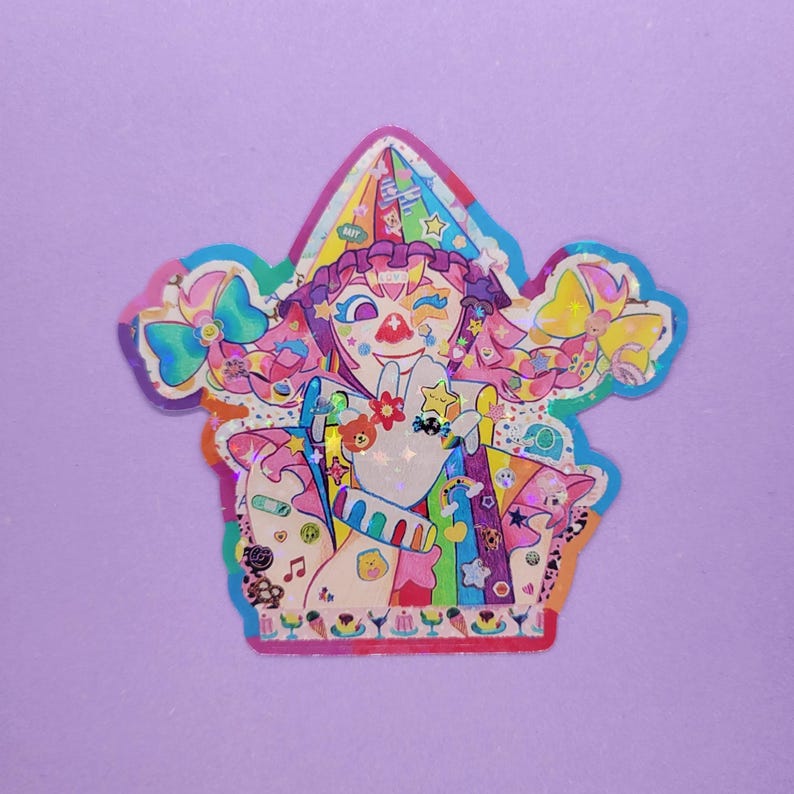 May include: A colorful sticker featuring a whimsical illustration of a clown-like character with rainbow hair, a star-shaped eye, and a red nose. The sticker has a holographic finish and is surrounded by a light blue border. The character is holding up a hand with various charms.