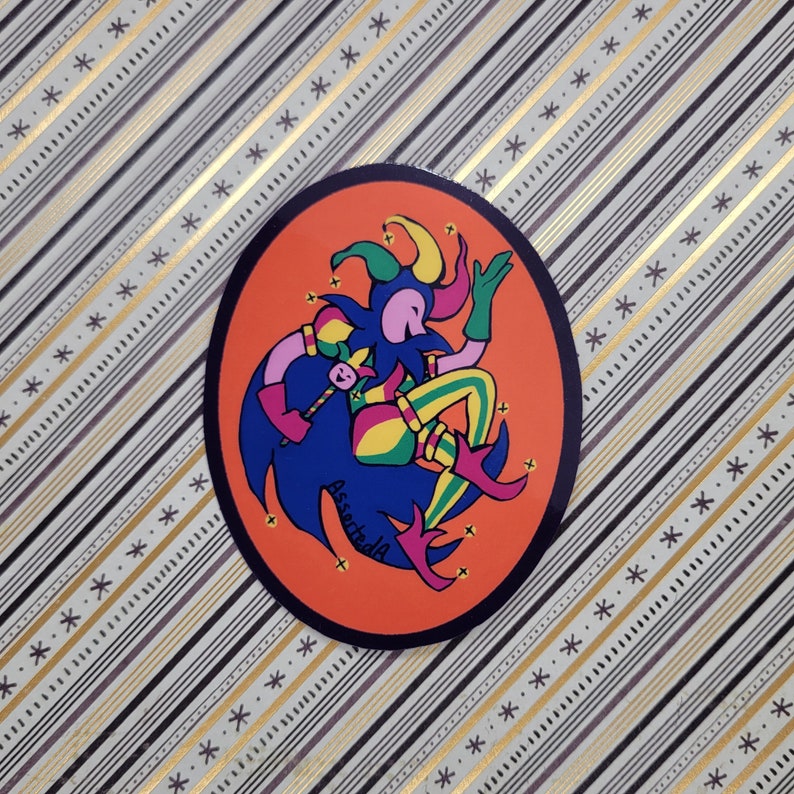 Op de afbeelding: Een ronde sticker met een oranje achtergrond waarop een nar in een blauw, groen en geel kostuum met een rode hoed en belletjes te zien is. De nar houdt een toverstaf vast en is omringd door sterren. De tekst "AssertedA" staat in het zwart onderaan de sticker.
