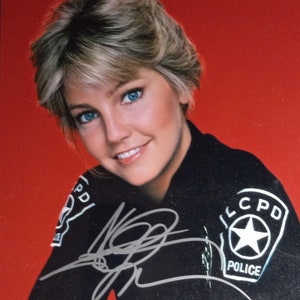 Puede incluir: Una mujer con cabello rubio lleva un uniforme de policía negro con una insignia que dice "LCPD POLICE". Ella sonríe y mira a la cámara. La foto está firmada.