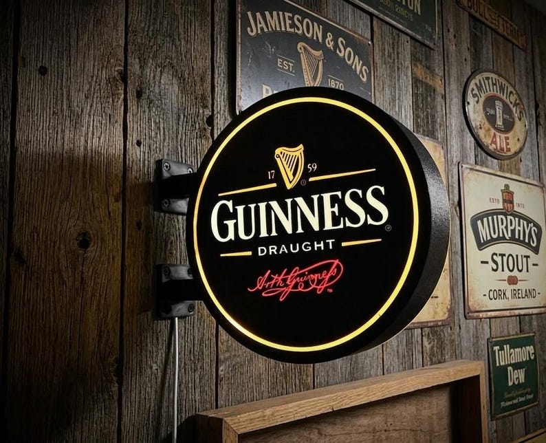 May include: A black and yellow Guinness Draught sign with the brand's logo, including a harp, is mounted on a wooden wall. The sign is round and illuminated, with the text "Guinness Draught" in white. Other vintage signs are visible.