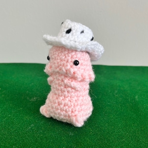May include: A pink crocheted amigurumi toy wearing a white crocheted cowboy hat with black polka dots.