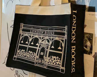 May include: Black canvas tote bag with white straps and a white outline of a storefront with the text "LONDON BOOKS" above the entrance. The text "LONDON BOOKS" is in gold lettering on the side of the bag.