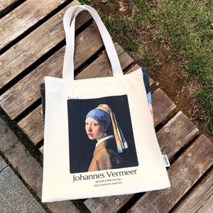 Puede incluir: Bolsa de tela blanca con una impresión del cuadro de Johannes Vermeer "La joven de la perla". El texto "Johannes Vermeer" y "Girl with a Pearl Earring 1665 Canvas Oil Painting" está impreso debajo de la imagen.