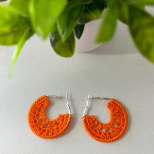 May include: A pair of orange crocheted hoop earrings with silver hoops.