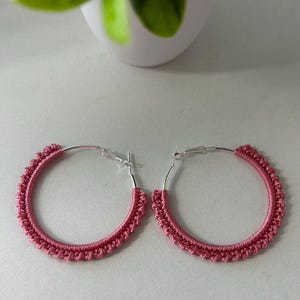 May include: A pair of pink crocheted hoop earrings with silver hoops.