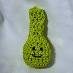 May include: A handmade, lime green crocheted pouch with a smiling face embroidered in black thread. The pouch has a small loop at the top and is likely used for small items or as a decorative item. The texture of the crochet is clearly visible.