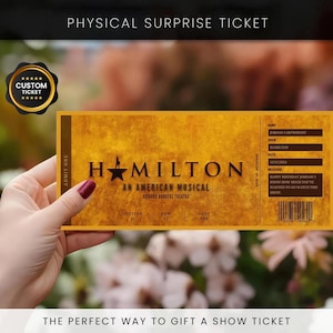 Op de afbeelding: Een gepersonaliseerd ticket voor de musical Hamilton, met een goud-bruin ontwerp. Het ticket bevat de naam van de show, de datum en een gepersonaliseerde boodschap. De tekst "Physical Surprise Ticket" staat bovenaan.