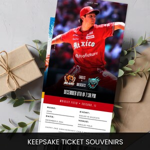 Pu&ograve; includere: Un souvenir di biglietto da baseball con un design rosso e nero. Il biglietto presenta un giocatore di baseball con una maglia rossa, i loghi delle squadre Eagles e Wildcats e il testo "DECEMBER 8TH @ 7:30 PM". Il testo "KEEPSAKE TICKET SOUVENIRS" &egrave; in basso.
