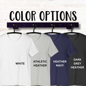 May include: Four t-shirts hanging on a rack, showing different colour options: white, athletic heather, heather navy, and dark grey heather.