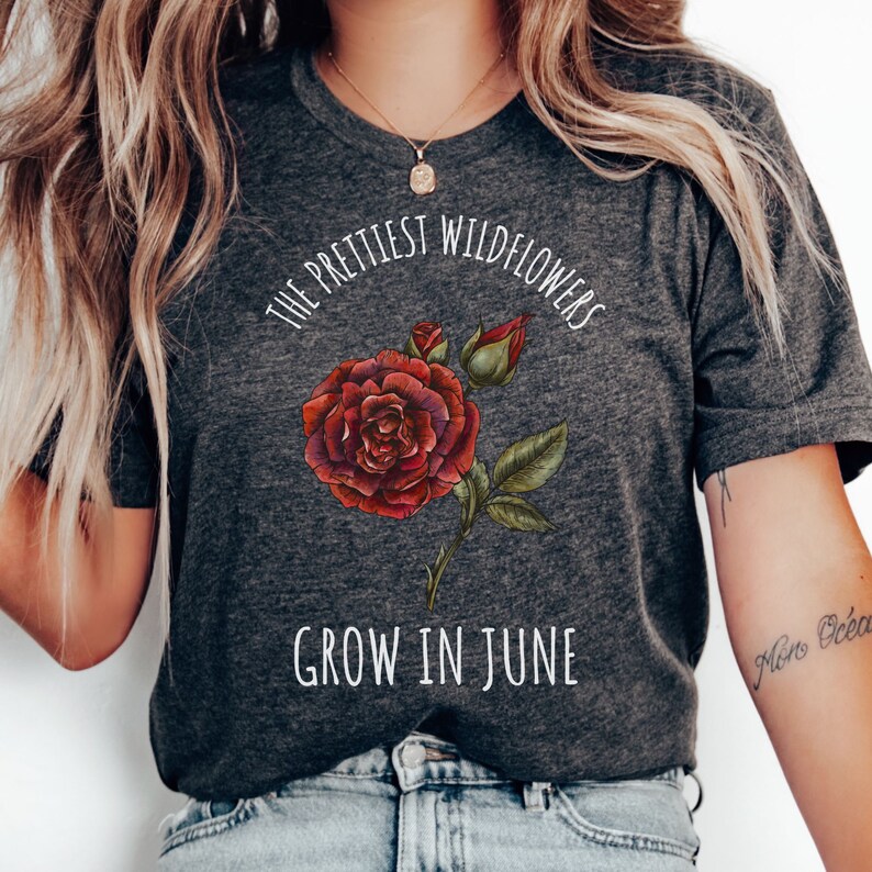 May include: A dark grey t-shirt with a white graphic design featuring a red rose and the text "The prettiest wildflowers grow in June."