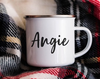May include: White enamel mug with a silver rim and a black handwritten name "Angie" on the front. The mug is sitting on a red and white plaid blanket.