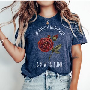 May include: A navy blue t-shirt with a white graphic of a red rose and the text "The prettiest wildflowers grow in June."
