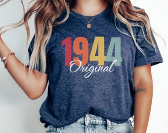 May include: Navy blue t-shirt with the year "1944" in colorful block letters and the word "Original" in white script. The shirt is a casual style, suitable for everyday wear.