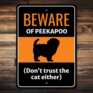 May include: A black and white metal sign with orange text that reads "Beware of Peekaboo (Don't trust the cat either)". The sign features a black silhouette of a dog.