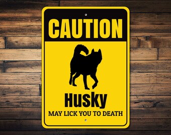 May include: Yellow and black caution sign with a silhouette of a husky dog. The sign reads "CAUTION Husky MAY LICK YOU TO DEATH."