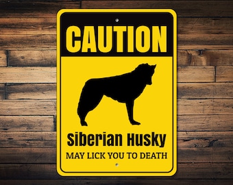May include: Yellow and black caution sign with a silhouette of a Siberian Husky. The sign reads "CAUTION Siberian Husky MAY LICK YOU TO DEATH."