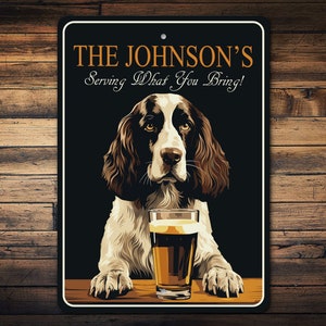 May include: A black and white sign with the text "THE JOHNSON'S Serving What You Bring!" and a brown and white dog with a glass of beer in front of it.