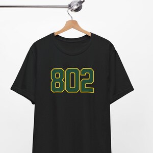 May include: Black t-shirt with a green and yellow number "802" printed on the front.