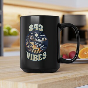 Può includere: Tazza da caffè in ceramica nera con una grafica bianca di una scena di spiaggia e il testo "843 VIBES".