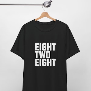 Può includere: Maglietta nera con testo bianco che dice "EIGHT TWO EIGHT"