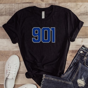 May include: Black t-shirt with a blue and white number 901 printed on the front. The shirt is paired with blue jeans and white sneakers.