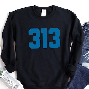May include: Black crew neck sweatshirt with the number "313" in blue block letters. The sweatshirt is paired with blue jeans and grey trainers with white laces. The items are arranged on a white surface.