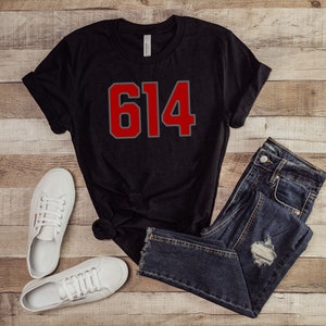 May include: Black t-shirt with a red and gray number 614 printed on the front. The shirt is paired with blue jeans and white sneakers.
