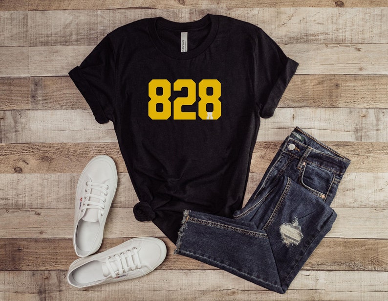 May include: Black t-shirt with a yellow number "828" printed on the front. The shirt is paired with blue jeans and white sneakers.