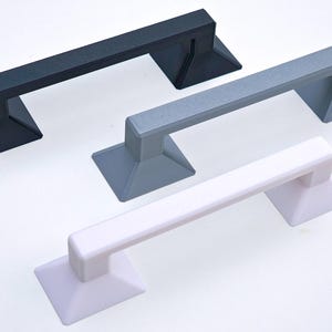May include: Three 3D printed handles in black, gray, and white. Each handle has a rectangular shape with a raised lip on each end. The handles are designed to be mounted on a surface.