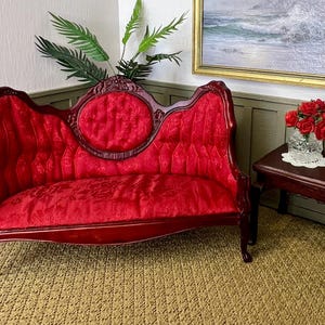 May include: A red velvet tufted sofa with ornate wooden carvings and cabriole legs. The sofa is in a room with a wooden table and a vase of red roses.