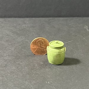 May include: A small green ceramic crock with a lid and two handles. The crock is about the size of a US penny.