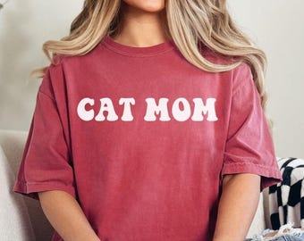 Könnte beinhalten: Ein rotes T-Shirt mit dem Text "CAT MOM" in weißen Retro-Lettern.