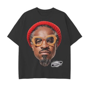 Op de afbeelding: Zwart T-shirt met een portret van een man met een rode muts en een grote, lichtgekleurde bril. De afbeelding bevat een logo met de tekst "VINTAGE ORIGINS". Het T-shirt is een klassieke ronde hals.