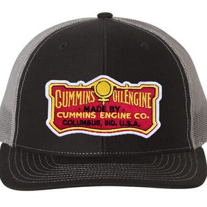 May include: A black and gray trucker hat with a red, yellow, and white embroidered patch that reads "Cummins Oilengine Made By Cummins Engine Co. Columbus, Ind. U.S.A."