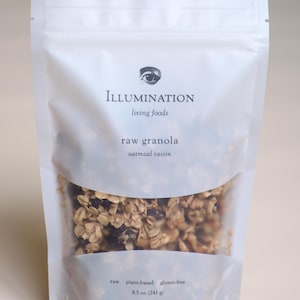Pu&ograve; includere: Un sacchetto bianco richiudibile di granola cruda con una finestra trasparente. La borsa presenta il testo "ILLUMINATION living foods" e "raw granola oatmeal raisin". La borsa contiene 241 g di granola ed &egrave; etichettata come cruda, vegetale e senza glutine.
