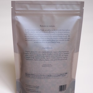Puede incluir: Una bolsa resellable de color claro con ingredientes org&aacute;nicos, incluyendo avena, almendras y ar&aacute;ndanos. La bolsa presenta texto sobre los ingredientes y la informaci&oacute;n nutricional del producto.