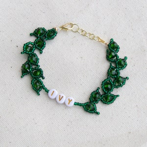 May include: A handmade bracelet featuring a green beaded ivy leaf design. The bracelet includes the word "IVY" spelled out in white letter beads. The clasp and chain are gold-colored, and the bracelet is displayed on a neutral background.
