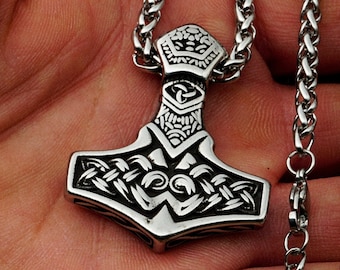 May include: A silver Mjolnir pendant necklace with intricate knotwork designs. The pendant is attached to a silver chain.