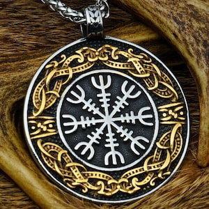 Peut inclure: Un collier avec un pendentif en argent et or, avec un pendentif circulaire noir orné d'un symbole Vegvisir blanc entouré d'un motif de nœud celtique doré.