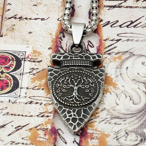 May include: Silver necklace with a pendant shaped like an arrowhead. The arrowhead has a textured surface and a tree of life design in the center.
