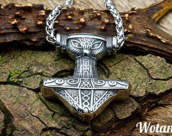 May include: Silver Mjolnir pendant necklace with intricate knotwork and a wolf's head design. The pendant is on a braided chain and resting on a piece of wood. "Wotancraft" is written in the bottom right corner of the image.