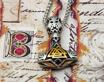 May include: A silver and gold pendant necklace featuring a detailed Mjolnir hammer design with a knotwork pattern. The pendant is on a silver chain.