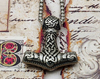 May include: Silver pendant necklace featuring a detailed Mjolnir hammer design with intricate knotwork. The pendant is on a silver chain.