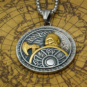 May include: A silver and gold pendant necklace featuring a Viking warrior holding an axe and shield. The pendant is detailed with intricate designs and is set against a map background.