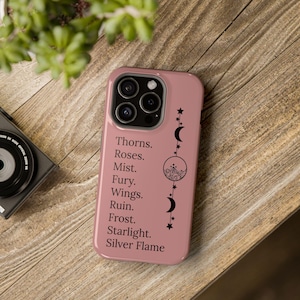 May include: A pink phone case with a black design featuring a crescent moon, stars, and the text "Thorns. Roses. Mist. Fury. Wings. Ruin. Frost. Starlight. Silver Flame."