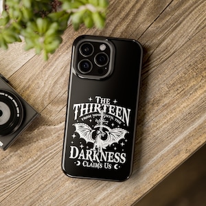 May include: Black phone case with a white design featuring a dragon, a cross, and the text "The Thirteen From Now Until The Darkness Claims Us".