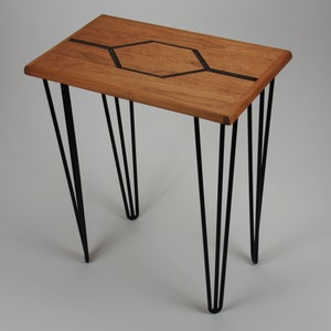 Peut inclure: Une petite table en bois avec un motif géométrique incrusté sur le dessus. La table a quatre pieds en épingle à cheveux noirs.