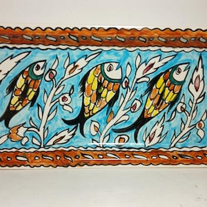 May include: A rectangular ceramic serving platter featuring a hand-painted design of three fish swimming among white leafy branches against a bright blue background, all enclosed within a decorative orange and white scalloped border.