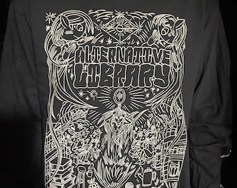 May include: Black long-sleeve shirt with a white graphic design featuring a whimsical illustration of a group of figures gathered around a campfire. The text "ALTERNATIVE LIBRARY" is prominently displayed in a stylized font. The bottom of the design reads "BELLINGHAM, WASHINGTON, USA."